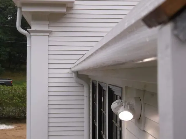 White house exterior with column, gutter, and a lit security light.