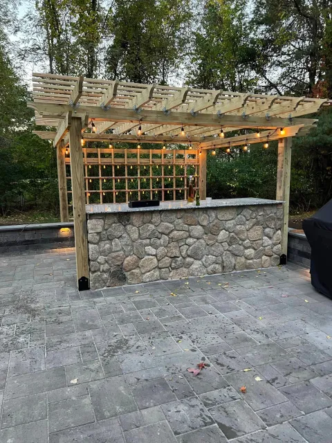 a wooden pergola over a stone bar on a patio .