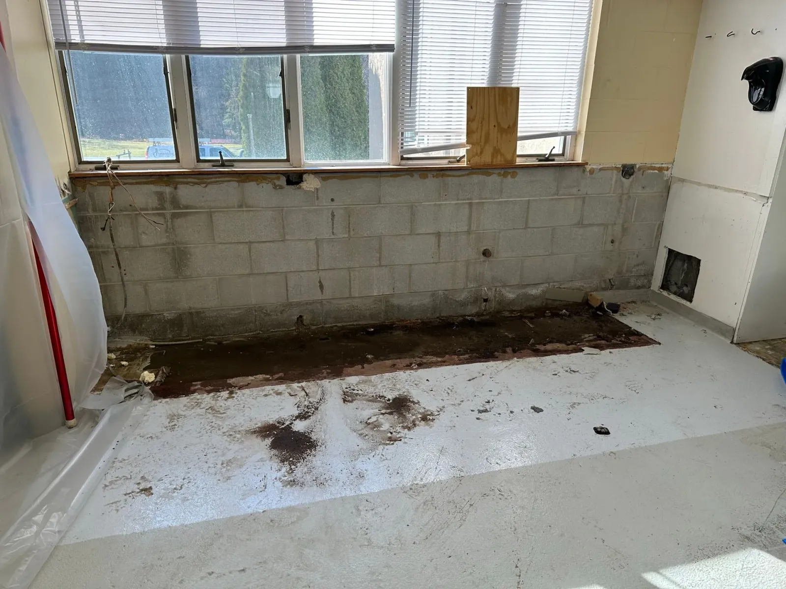 Interior room with exposed concrete wall, debris on the floor, and windows with blinds above.