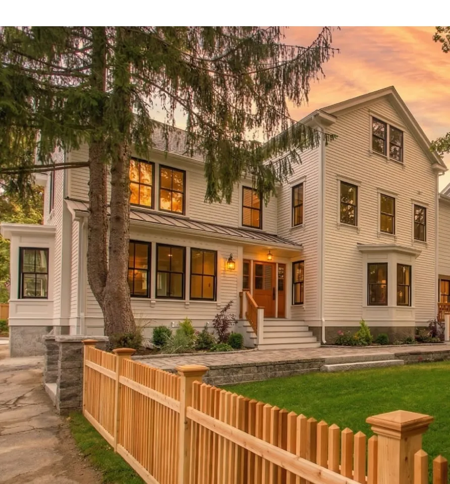 17 Smith Place: Two-story white house with black-trimmed windows, a wooden porch, green lawn, and a wooden picket fence at sunset.
