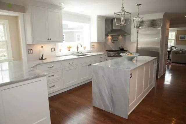 Bright modern kitchen with white cabinets, marble island, stainless steel appliances, and hardwood floors
