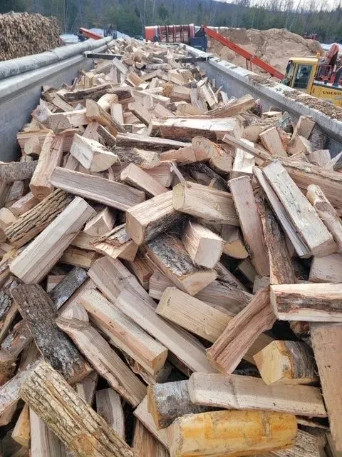 Piled split firewood on a flatbed truck with red safety rails along a roadside