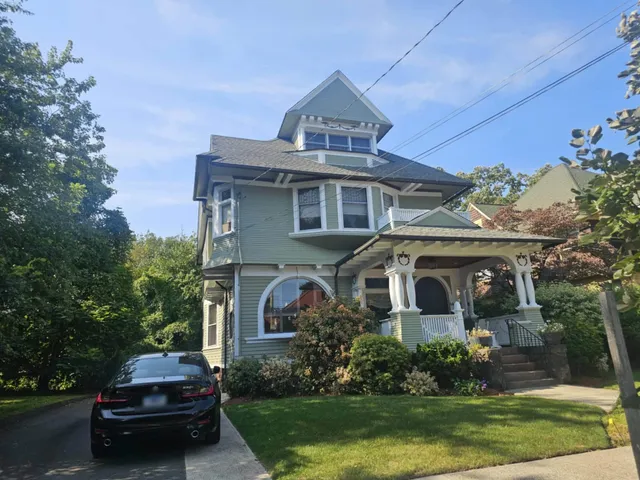 Front of the finished three-story house in sage green with white trim and a wraparound porch