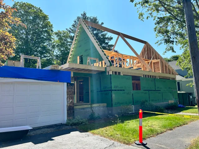 Custom home construction in Wakefield, MA, featuring engineered roof trusses, ZIP sheathing, and a partially completed exterior with blue tarp covering.