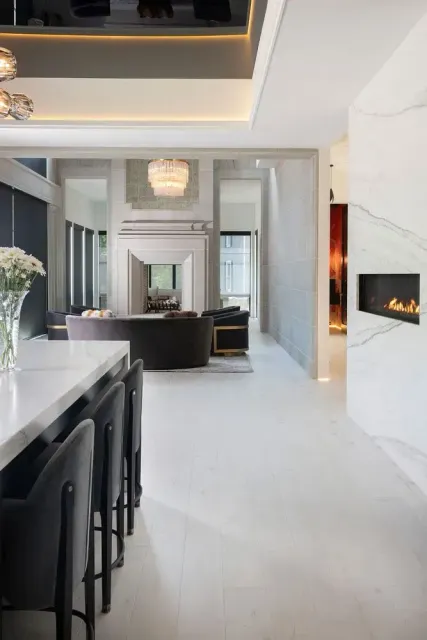 Modern interior with marble fireplace, kitchen island, and seating leading to a living room.