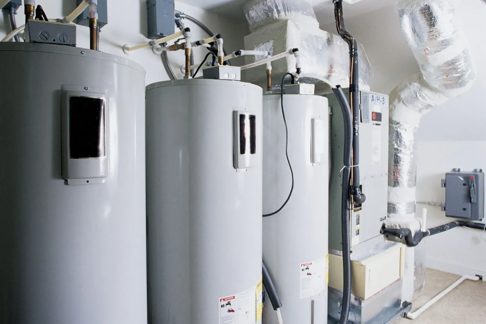 Three water heaters in a utility room, with associated ductwork and controls.