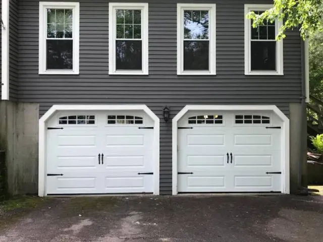 Two white garage doors are on the side of a gray house.