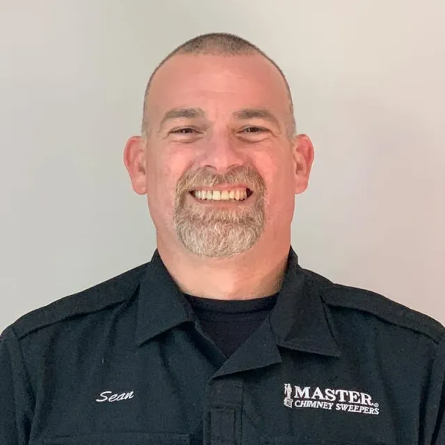 A man with a beard is wearing a black shirt and smiling.