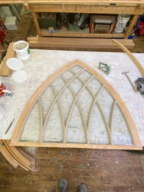 View from above of a woodworking project in progress, showing a wooden frame with a lattice design on a workbench, with tools and supplies around.