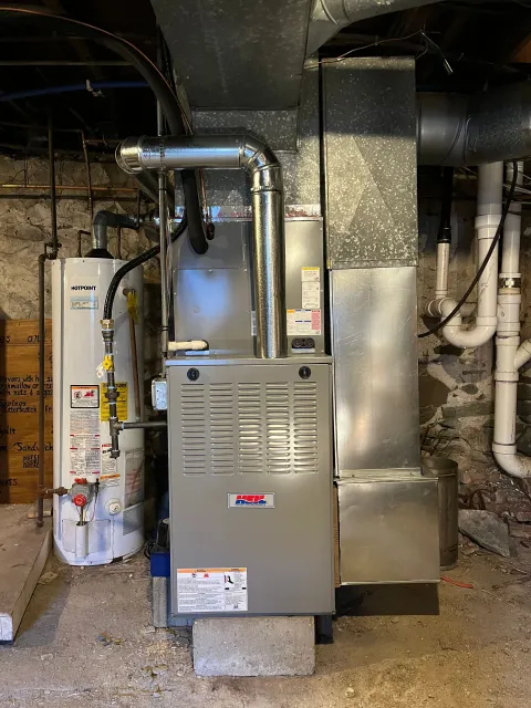 An air conditioner is sitting in a basement next to a water heater.