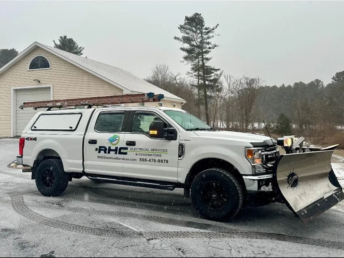 A white truck with a snow plow on the back is parked in front of a garage.