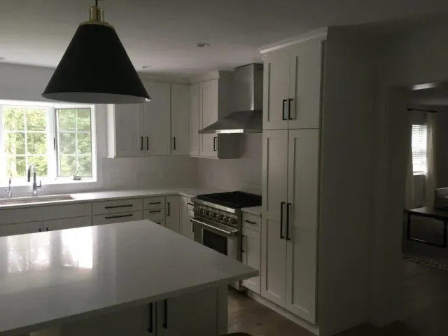 Bright modern kitchen with white cabinets, island, black pendant light, and sunlit window