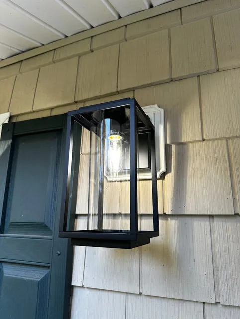 Modern Black Outdoor Wall Light Fixture with a Clear Glass Cover Installed on the Side of a House