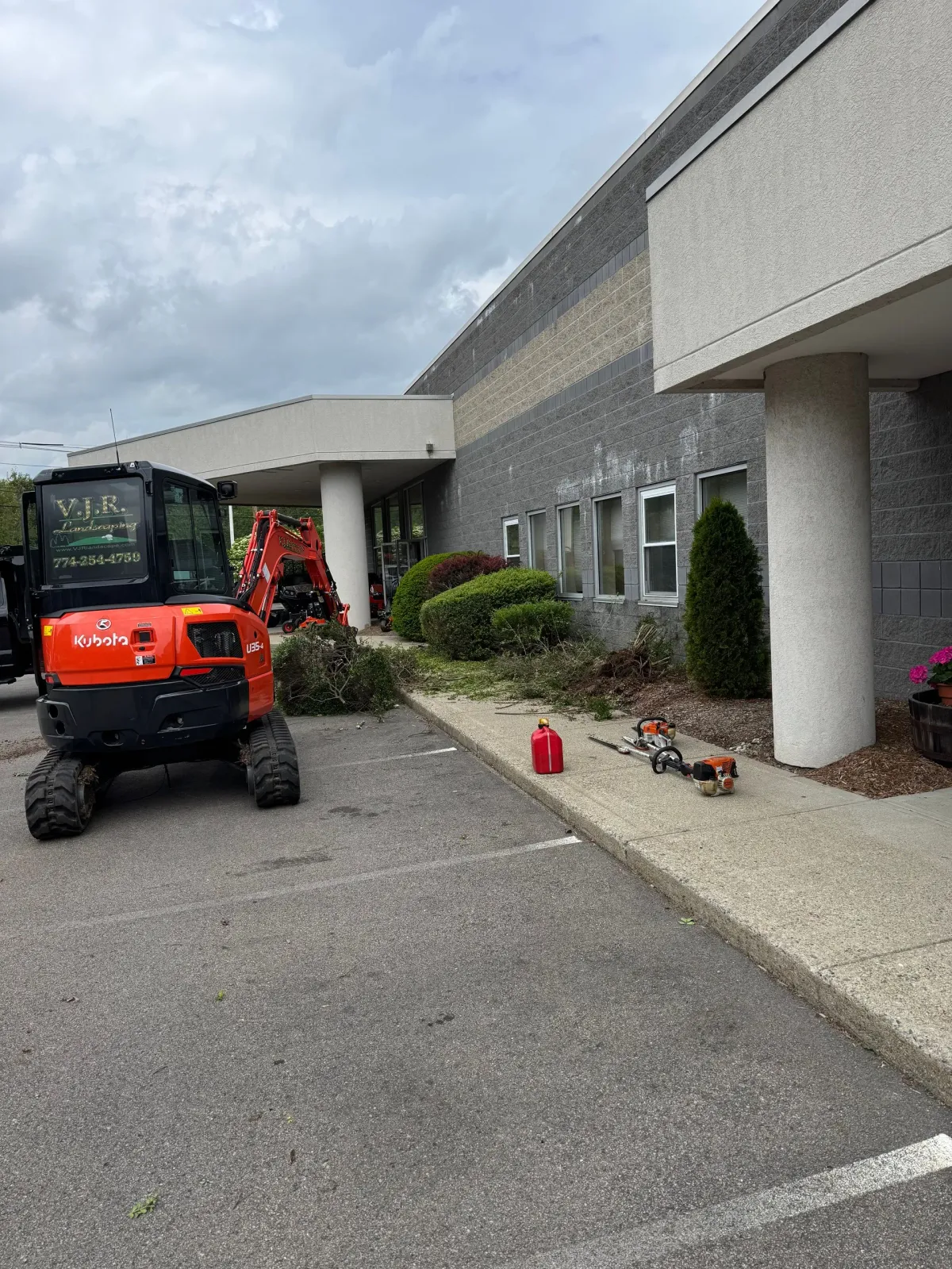 Red utility vehicle and landscaping equipment beside a building with trimmed bushes.