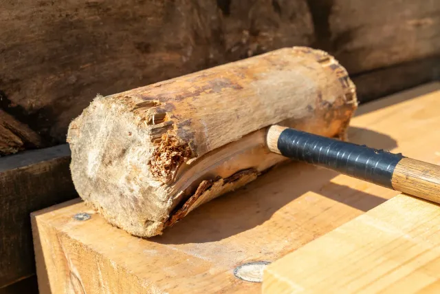 A wooden log is being hammered with an axe on a workbench.