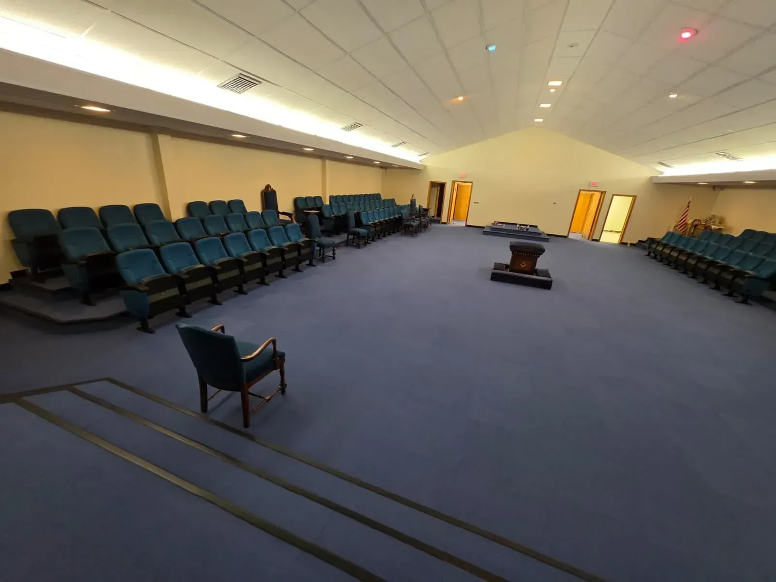 Empty auditorium with blue carpet, teal seats, and a small table in the center.
