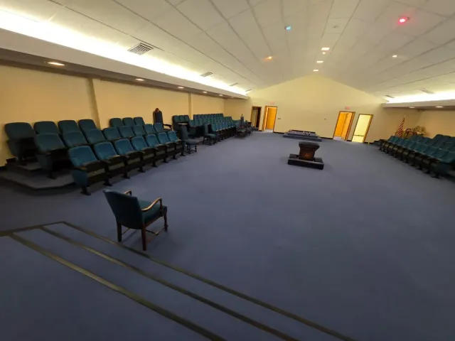 Empty auditorium with blue carpet, teal seats, and a small table in the center.