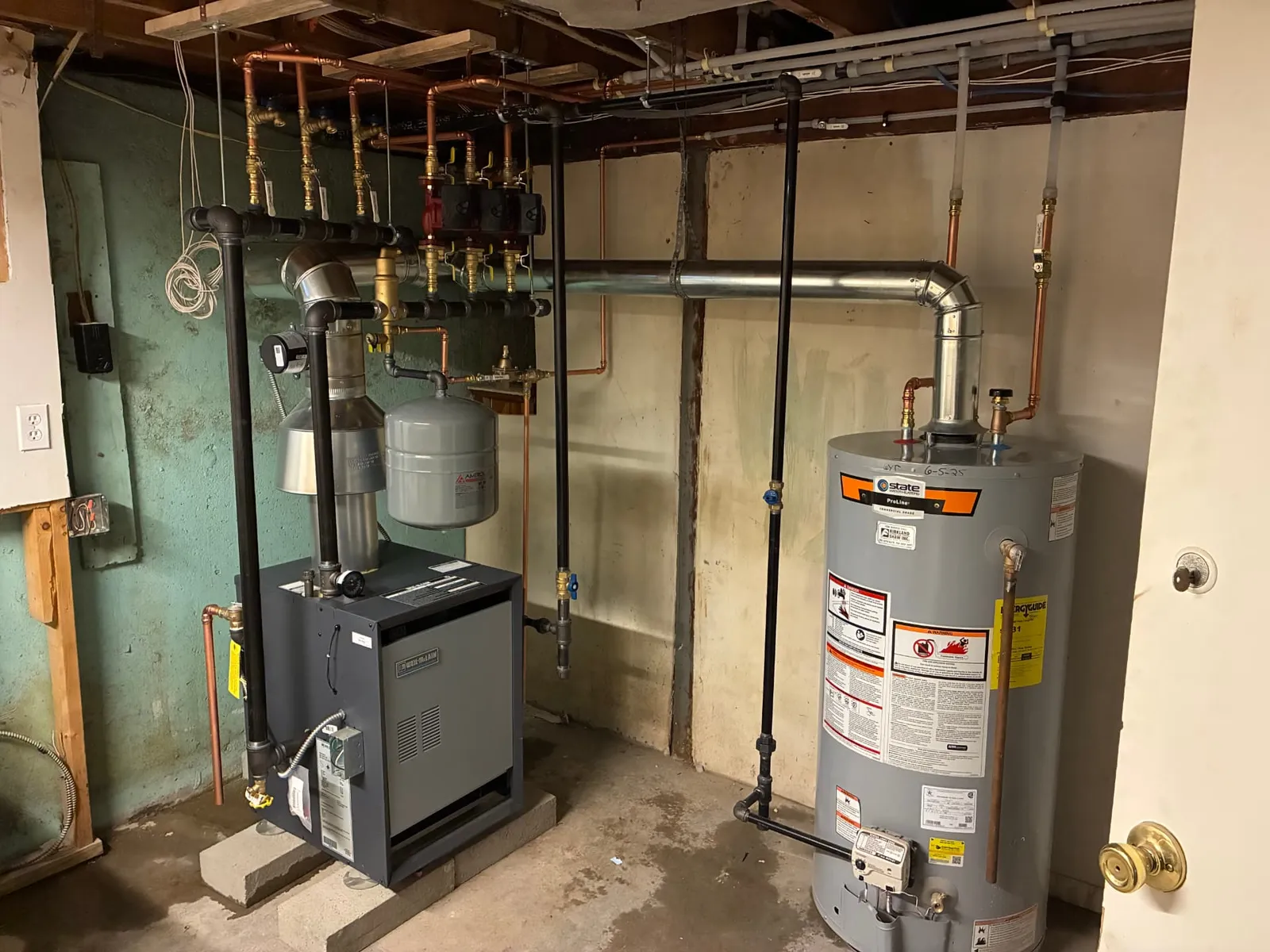 Gas water heater installed next to a boiler with copper and black iron piping in Acton, MA by Top Shelf Plumbing & Heating