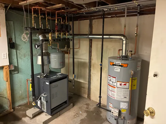 Gas water heater installed next to a boiler with copper and black iron piping in Acton, MA by Top Shelf Plumbing & Heating
