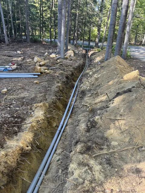 Two runs of gray PVC conduit laid in an open trench for an underground 200 amp electrical service