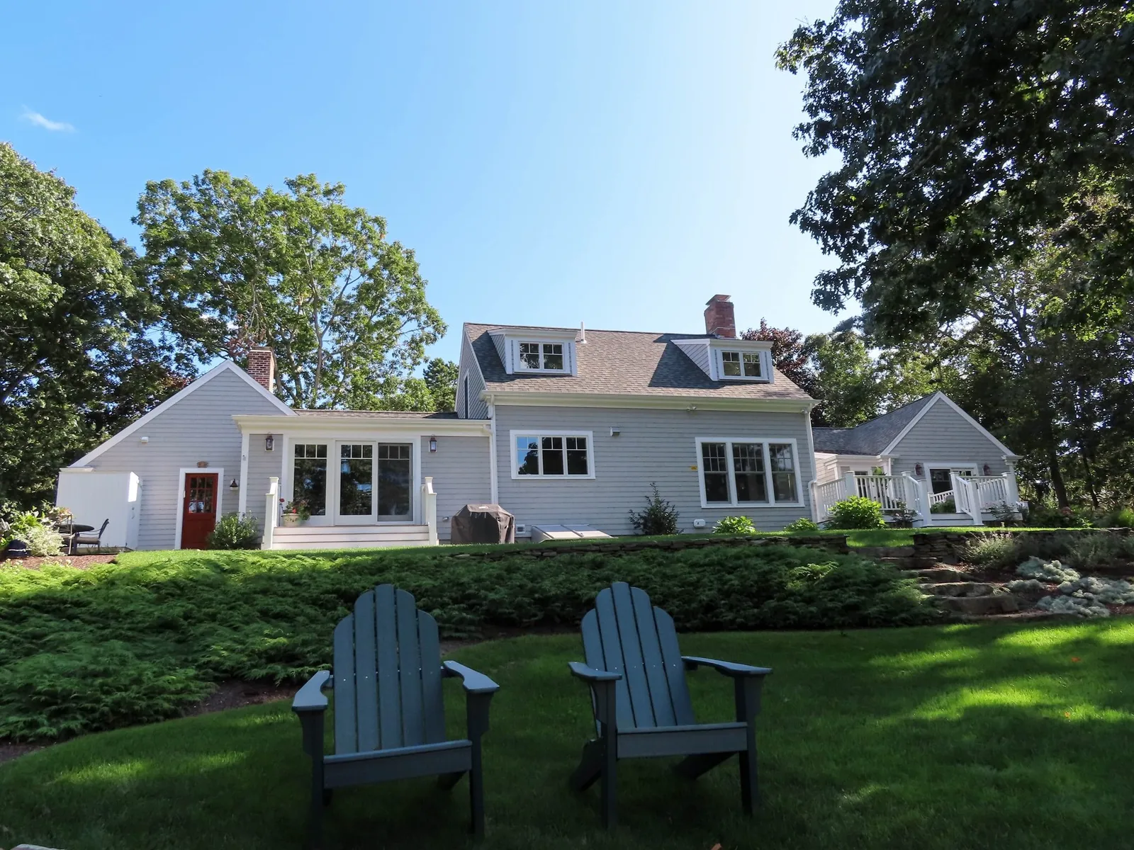Back yard of a sprawling home with 2 adirondack chairs