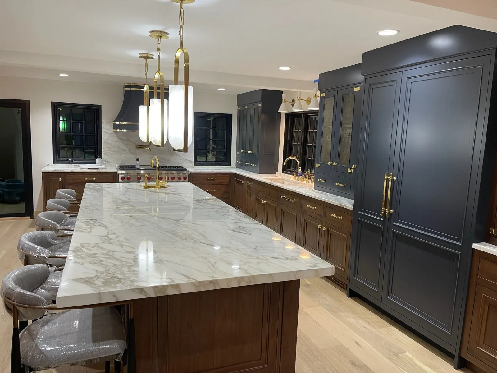 Modern kitchen with a large marble island, dark cabinets, gold hardware, and pendant lights.