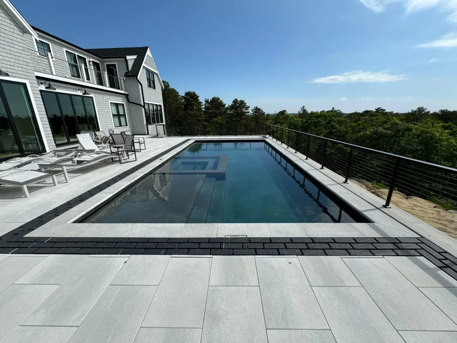 A modern house with large windows and a rooftop pool overlooking trees, under a blue sky with a few clouds.