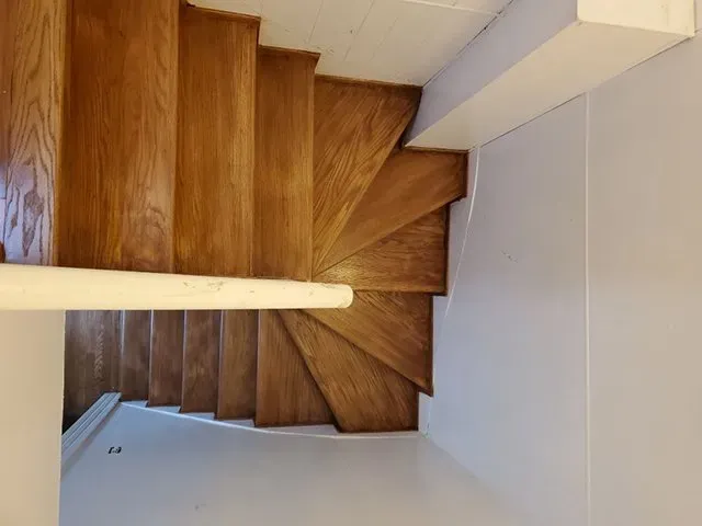 A wooden spiral staircase in a room with a white wall.