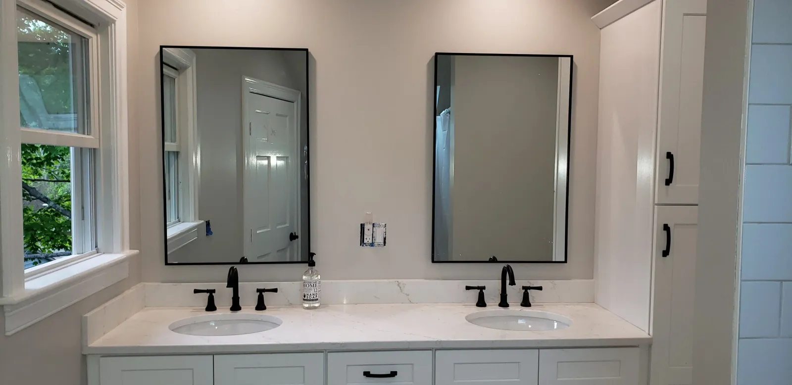 Modern bathroom with two rectangular mirrors, double sinks with black faucets, white marble countertop, white cabinets, and a soap dispenser.