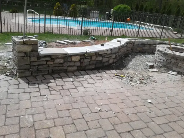 Pool surround with a natural stone seat wall and paver deck