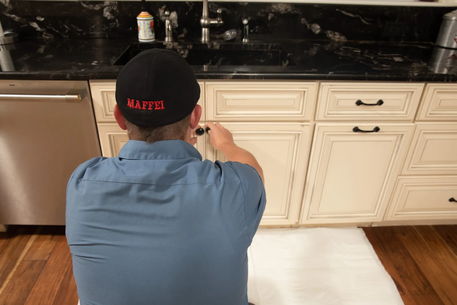 Maffei technician working under-sink kitchen plumbing on a drop cloth