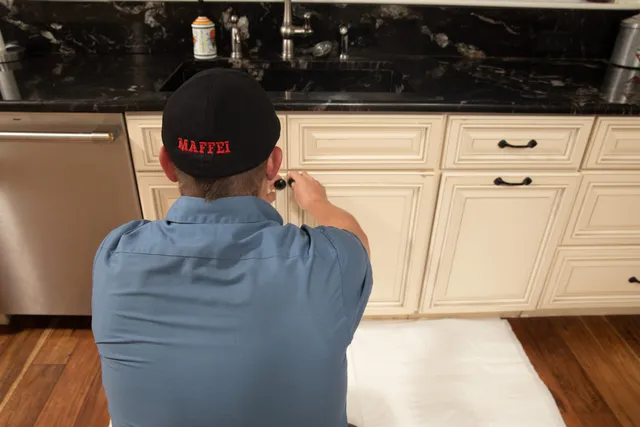 Maffei technician working under-sink kitchen plumbing on a drop cloth
