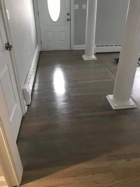 Hardwood floor in foyer with white door, radiator, and columns; light reflection on floor.