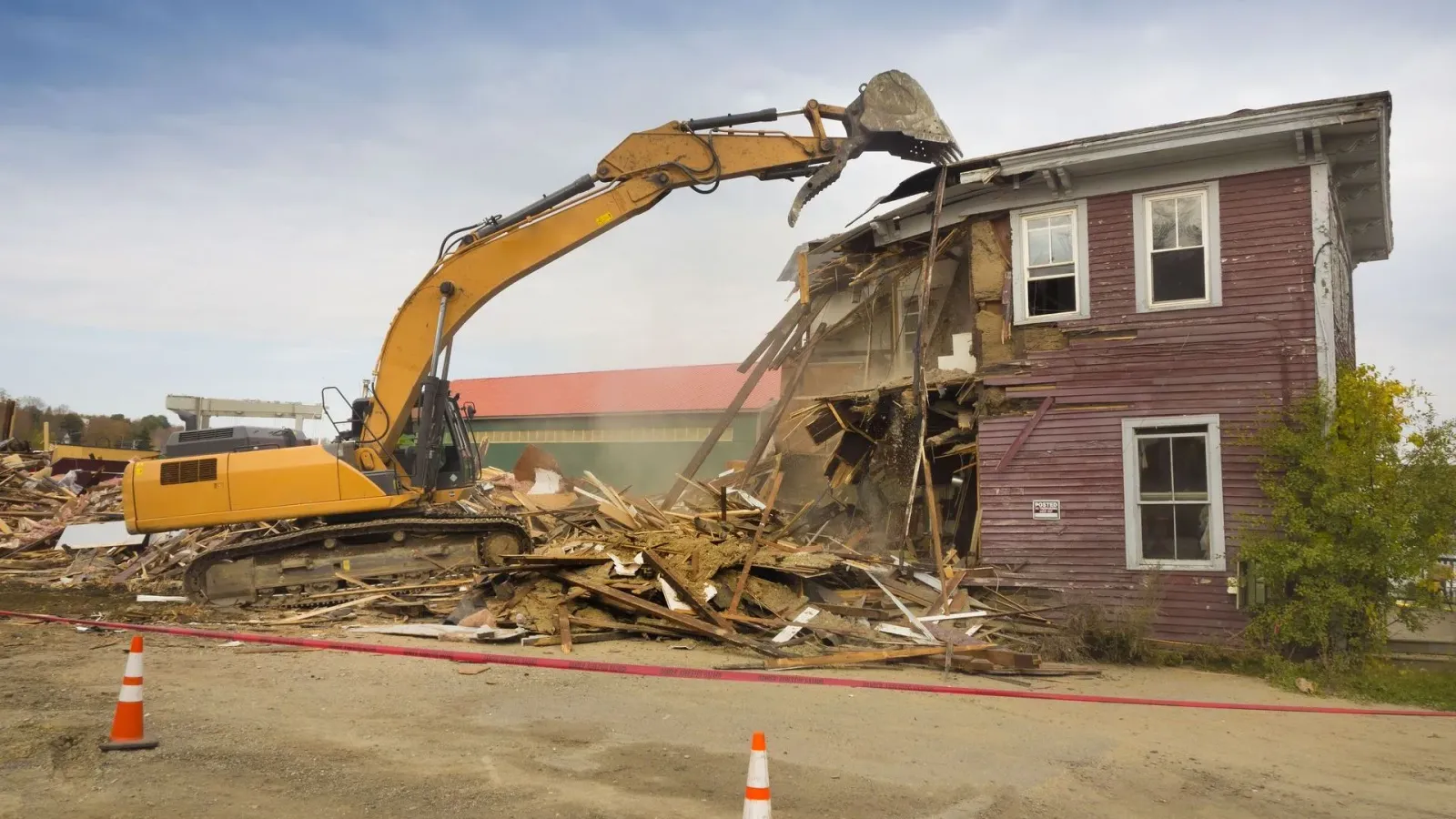 A yellow excavator is demolishing a red house.
