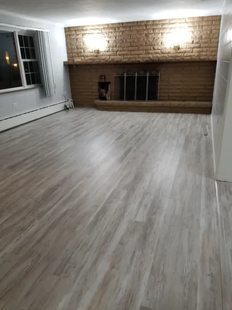 A large living room featuring light gray wood-look laminate flooring and a large brown stone fireplace.