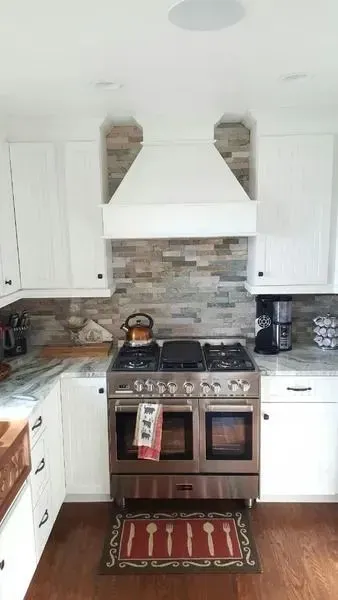 Bright kitchen with white cabinets, stainless steel stove, brick backsplash, and red rug.