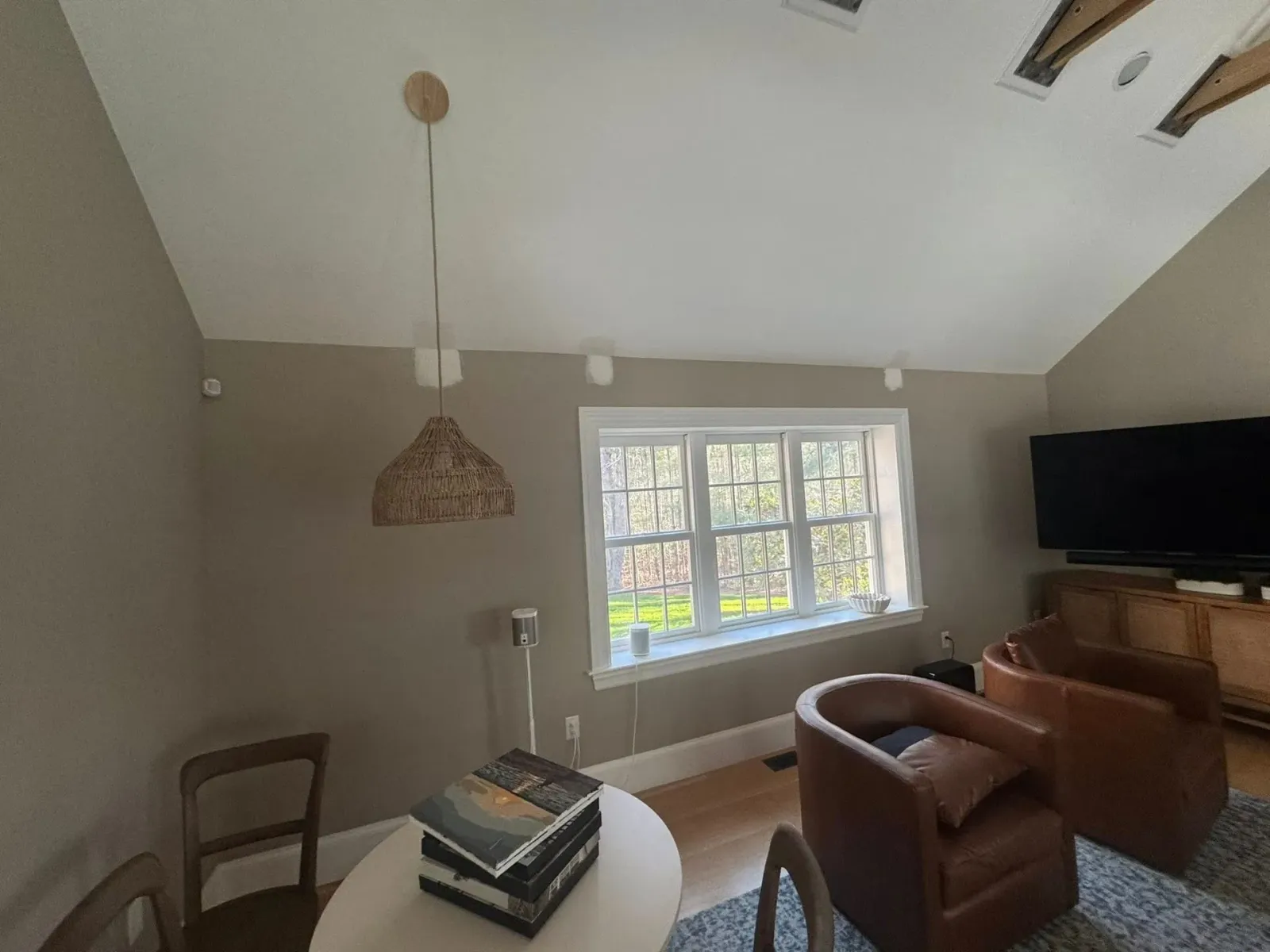 Cozy living room with a large window, brown chairs, a wall-mounted TV, and a woven pendant light.