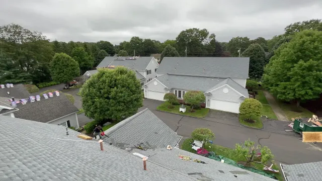 Elevated view of roofers replacing grey shingle roofs on Connecticut homes with a dumpster on site