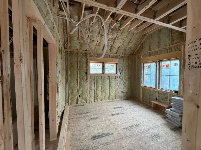 Unfinished room with exposed wood framing, insulation, and windows letting in daylight.