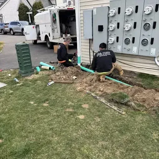 Plumber in blue overalls and gloves using a snake tool on an open sewer manhole.