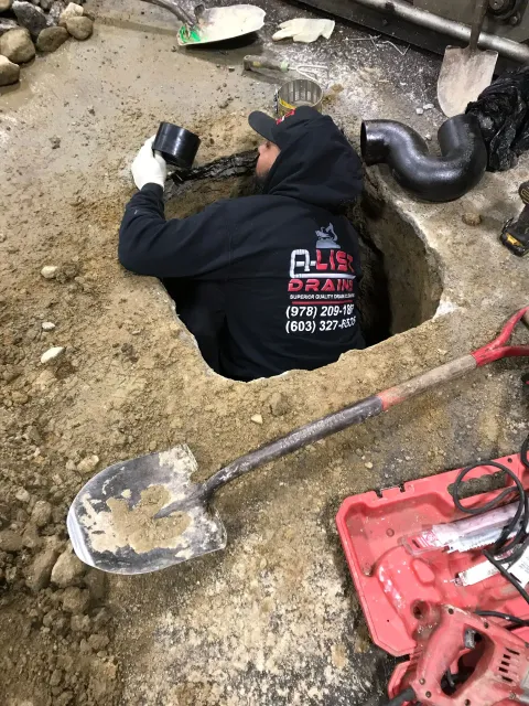 A man is crawling out of a hole in the ground with a shovel.