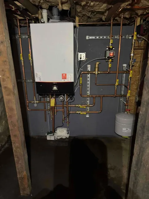 Utility room with a white boiler, exposed copper pipes, and a water tank on a gray wall.