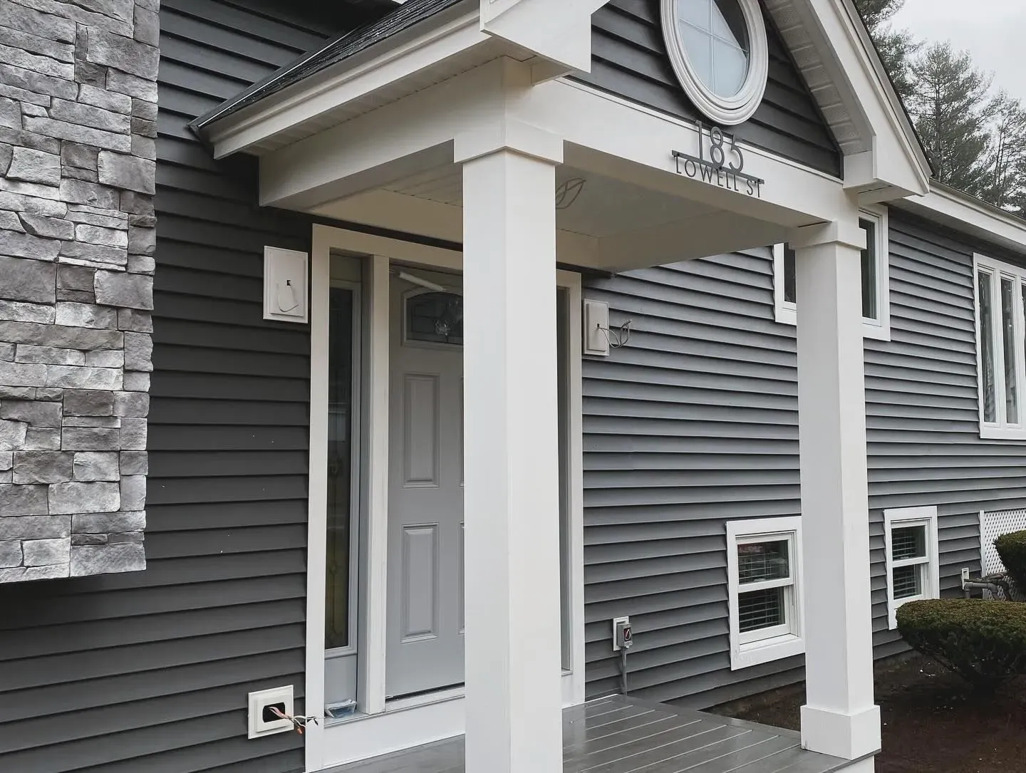 A gray house with a white porch and a clock on the front of it.