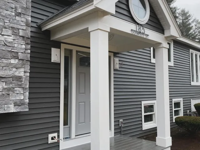A gray house with a white porch and a clock on the front of it.