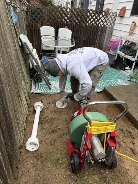 SOS technician clearing a drain line at an outdoor cleanout in Rhode Island