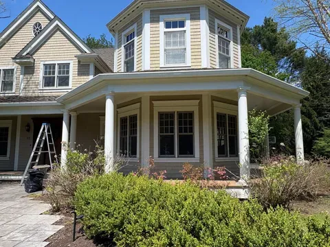 Victorian house with a wraparound porch, blue bay window, and front garden under a clear sky
