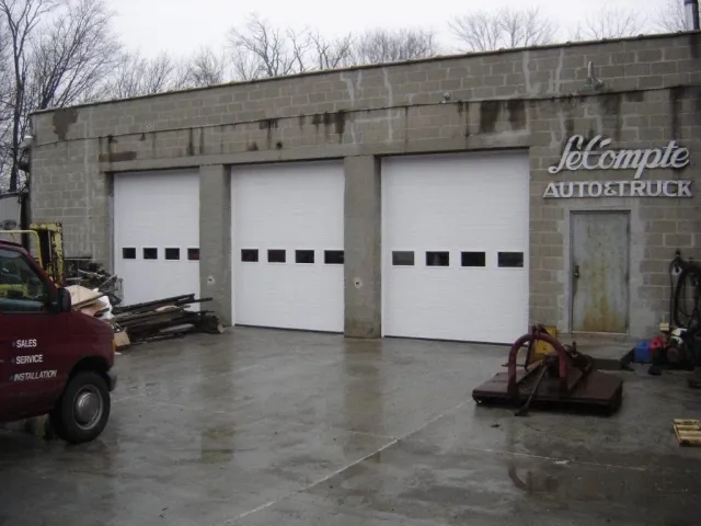 Exterior of a garage with three closed white doors and a sign that reads