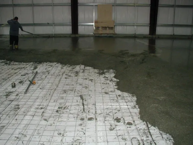 A man is spreading concrete on the floor of a building