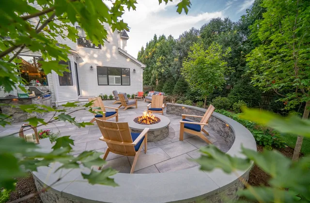 Backyard fire pit patio with curved seating wall and Adirondack chairs surrounded by lush plantings in Needham, Massachusetts by Land Design Associates.