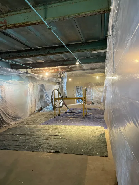 Construction site: interior view of a room with exposed beams, plastic sheeting, and scaffolding.
